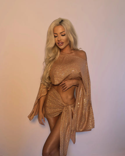 Donna Di Luxury's Blush Rosé resort two-piece, an off-shoulder tie-front top and wrap mini skirt finished entirely in hand-set crystals, photographed on a soft neutral background.